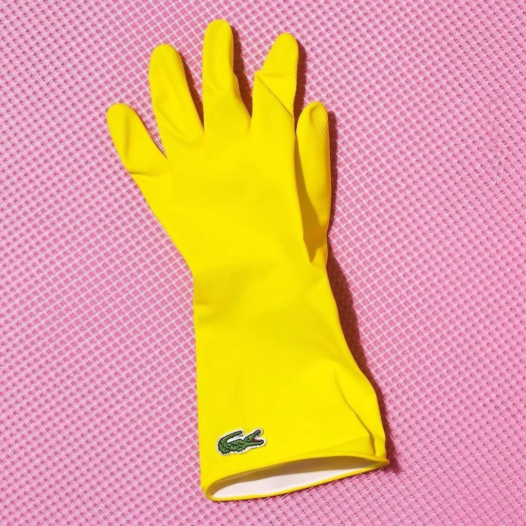 A yellow rubber glove laid flat on a hot pink field, one small badge at the cuff