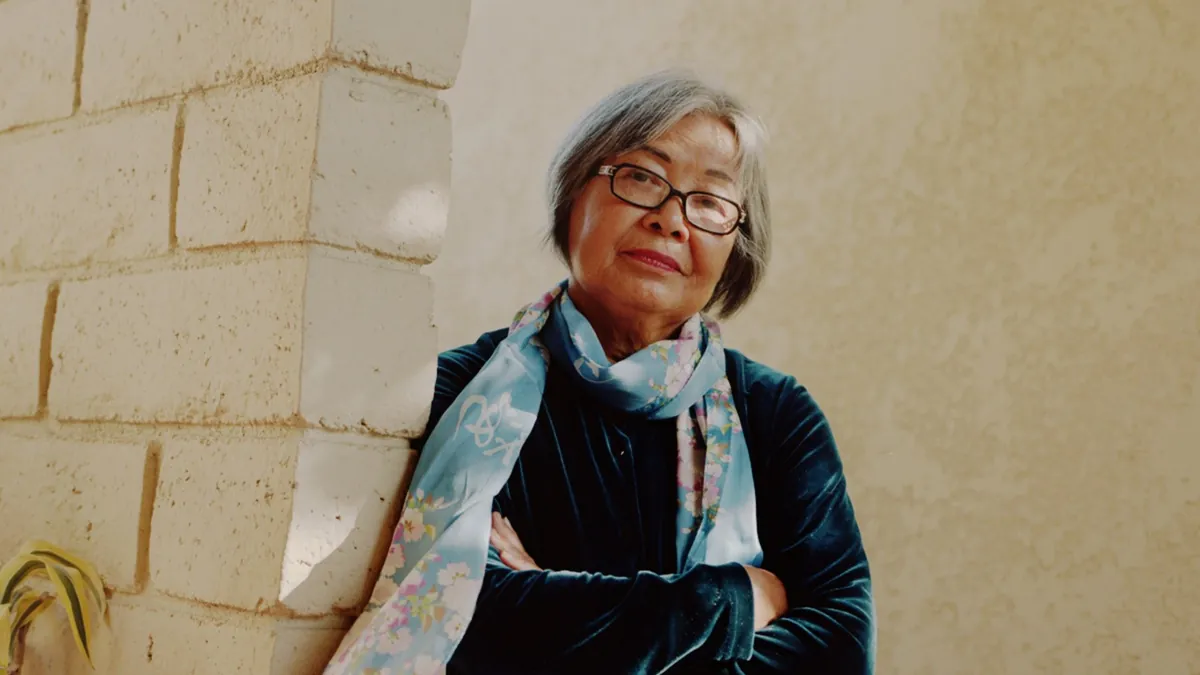 A woman in navy velvet leans on a pale stone wall, arms folded, in soft afternoon daylight