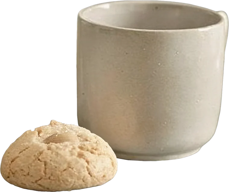 A cream stoneware mug beside an almond biscuit