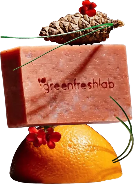 A bar of soap balanced on a halved orange, topped with a pine cone